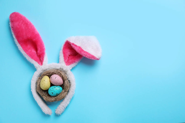 Headband with bunny ears, painted eggs and space for text on light blue background, flat lay. Easter holiday - Foto, afbeelding