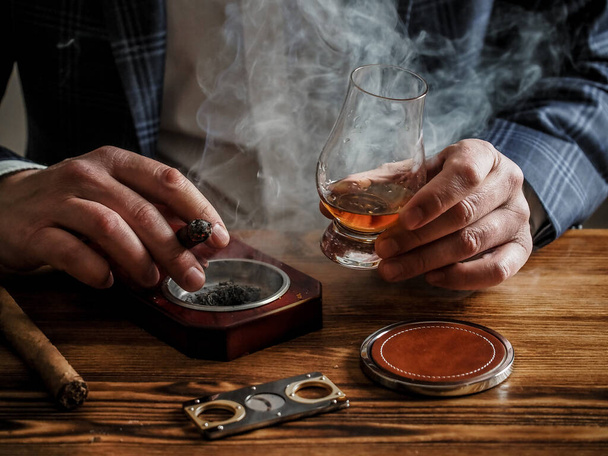 Um homem bem vestido em um bar bebe whisky malte único e fuma um charuto - Foto, Imagem