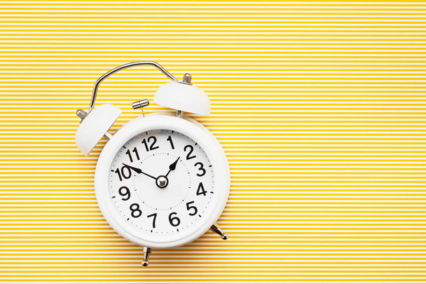 White vintage alarm clock on yellow background. Top view, copy space. Daylight saving concept. - Photo, Image