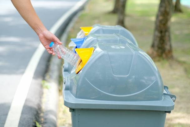Hand put plastic bottle to the gray bin in park or garden with day light. - Foto, Bild
