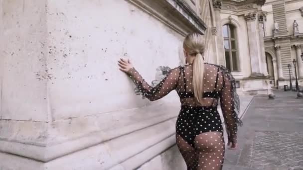 Jonge vrouw draagt een sexy transparante zwarte jurk tijdens het lopen in de straat in het historische centrum van Europa stad. Actie. Sexy aantrekkelijke blonde plus size model in chiffon jurk, achteraanzicht. - Video