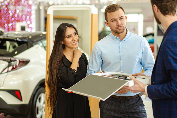 young couple choosing new car in showroom. service, selling - Фото, зображення