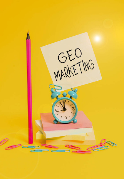 Writing note showing Geo Marketing. Business photo showcasing the geolocated marketing techniques to get new clients Alarm clock sticky note stacked notepads pencil colored background. - Foto, afbeelding