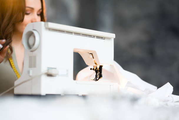 Beautiful woman sews clothes for buyers on a sewing machine - Fotoğraf, Görsel