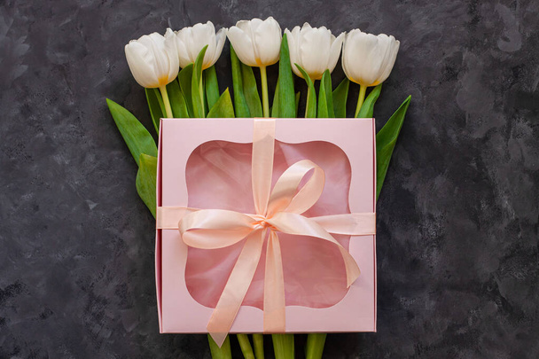 White tulip flowers and pink gift box with ribbon bow on dark background flat lay. Place for text 8 March Happy Womens Mothers Day.Flower Bouquet greeting card.Copy space website banner top view - Foto, Bild