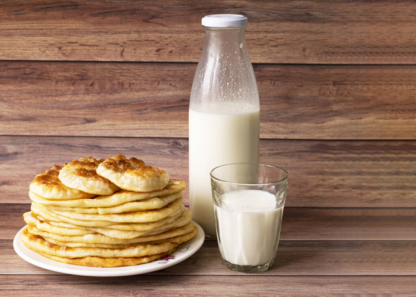Υγιεινή ρουστίκ τροφή. Γάλα σε μπουκάλι, ποτήρι και ζεστά κέικ για πρωινό. Σιτάρι, κέικ καλαμποκιού. Ξύλο - Φωτογραφία, εικόνα