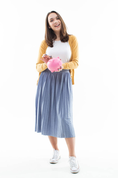 Meisje verzamelt geld in een roze spaarvarken bank op een witte achtergrond - Foto, afbeelding