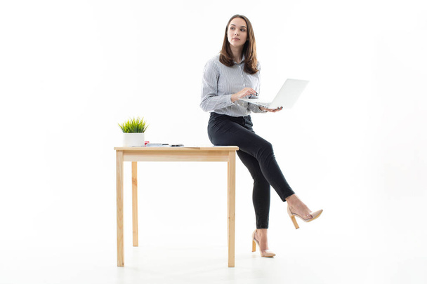 A girl is sitting on a table and typing on a computer on a white background - Foto, Imagen