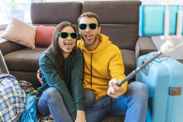 young couple sitting on the floor at home take a selfie between the suitcases before leaving for the holidays - Foto, Imagen