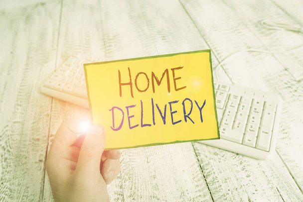 Handschriftlicher Text Home Delivery. Konzept bedeutet Akt der Übernahme von Waren oder Paketen direkt zu den Kunden nach Hause Mann hält bunte Erinnerung quadratische Papier weiße Tastatur Holzboden. - Foto, Bild