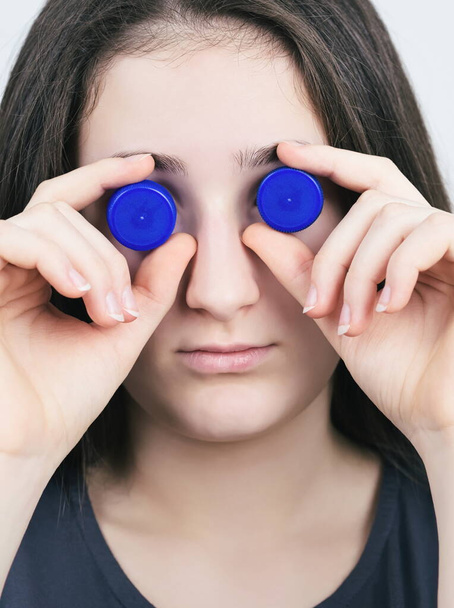Portrait of a Brunette Teen Girl with Blue Plastic Bottle Caps Closeup - Photo, Image