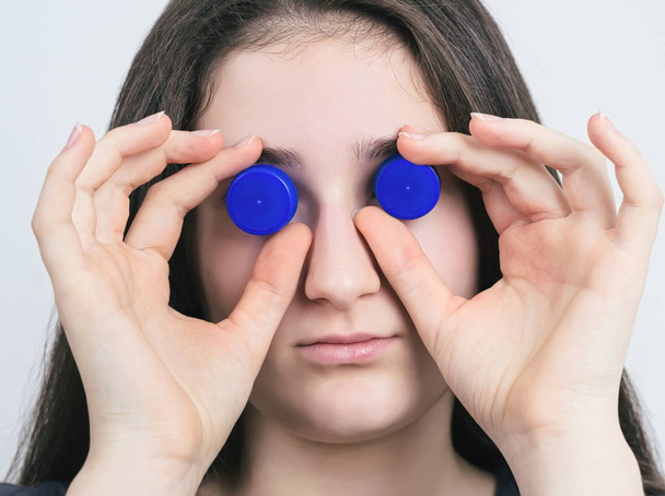 Portret van een Brunette tiener meisje met blauwe plastic fles Caps Closeup - Foto, afbeelding