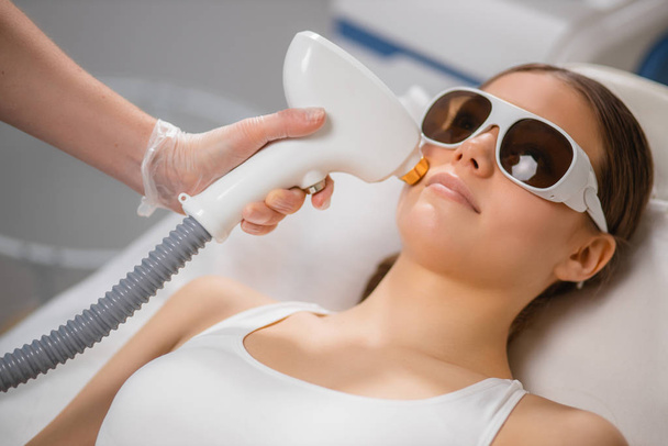 young woman receiving laser epilation treatment on face at beauty salon - Foto, Imagem