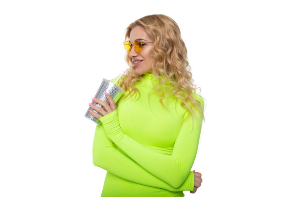 The blonde in a bright dress holds a glass for cocktail in hands on a white background - Photo, Image