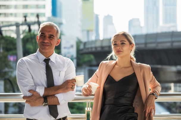 Senior American businessman and young beautiful business woman in uniform relax during coffee break outside the office buidling in modern city. Get fresh air to refreshment from hard project work. - Foto, Imagen