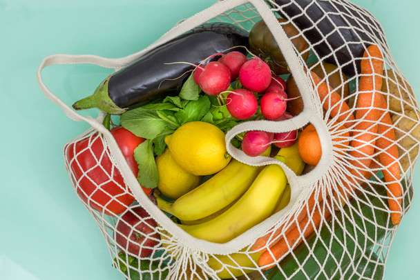 Legumes frescos e frutas em torno de uma malha de compras orgânica. conceito de ação consciente e amiga da natureza
 - Foto, Imagem