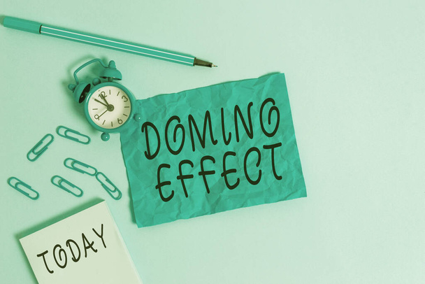 Handwriting text writing Domino Effect. Concept meaning Chain reaction that causing other similar events to happen Alarm clock clips notepad blank crushed sheet marker sky colored background. - Foto, afbeelding