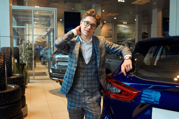man in glasses and fashion checked suit standing in light car dealership - Zdjęcie, obraz