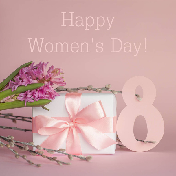 Caja de regalo blanca con cinta rosa, flor de jacinto, ramitas de sauce y número 8 sobre fondo rosa con texto. Feliz Día Internacional de la Mujer 8 de marzo tarjeta de felicitación. Imagen cuadrada
. - Foto, imagen