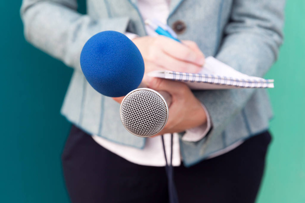News reporter or TV journalist at press conference, holding microphone and writing notes	 - Photo, image