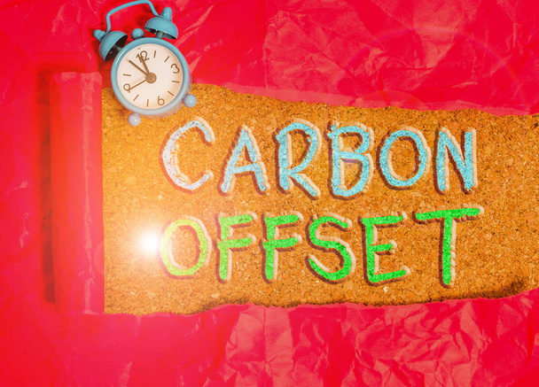 Teksti merkki osoittaa Carbon Offset. Käsitteellinen kuva Hiilidioksidin tai muiden kaasujen päästöjen vähentäminen Hälytyskello ja revitty pahvi sijoitettu puisen klassisen pöydän taustalle
. - Valokuva, kuva