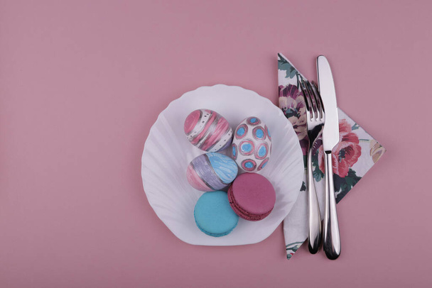 Easter eggs in a white plate near a napkin and a knife and a fork on a pink background - 写真・画像