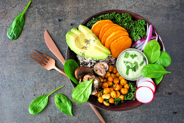 Healthy vegan lunch bowl with avocado, sweet potato, kale and vegetables. Top view on a dark stone background. Healthy eating concept. - Photo, Image