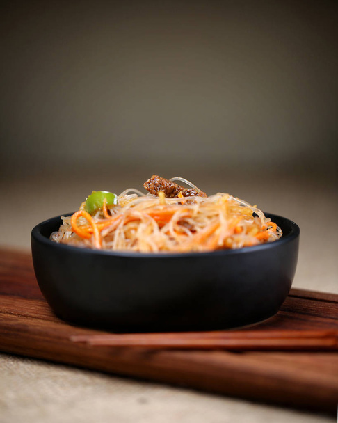 Glass noodle salad with meat and carrots in a black bowl on a wooden board - Φωτογραφία, εικόνα