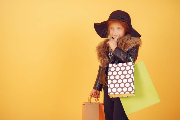 Cute little girl with shopping bags on a yellow background - Foto, Bild