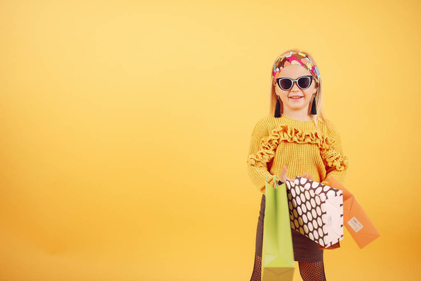 Cute little girl with shopping bags on a yellow background - Fotografie, Obrázek