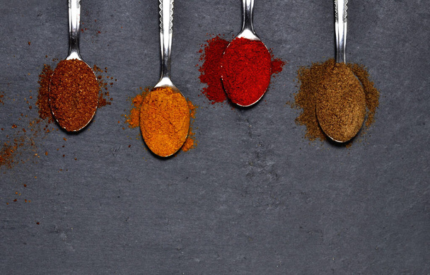 Teaspoons with spices - cumin, curry, sweet pepper, barbecue spices on slate plates. Top view. Copy space. - Фото, изображение