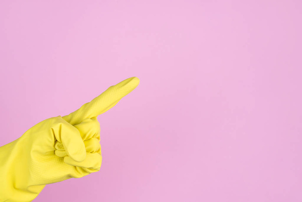 Fechar a foto da mão em luvas protetoras amarelas mostrando o dedo no espaço em branco isolado fundo pastel
 - Foto, Imagem
