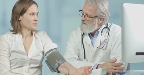 Médico en su consultorio midiendo la presión arterial de su paciente femenino
 - Imágenes, Vídeo