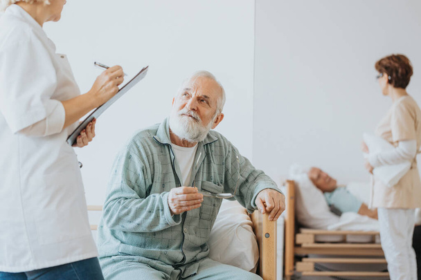 Senior doctor in a beige uniform talks to an elderly patient during a walk around hospital - 写真・画像