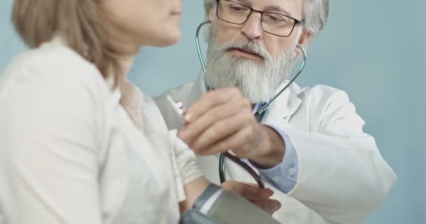 Medische arts in zijn kantoor meten puls van zijn vrouwelijke patiënt met zijn chique stethoscoop. 4k slow motion - Video