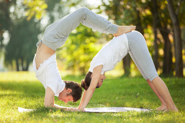 Couple Yoga, man and woman doing yoga exercises in the park - Photo, image