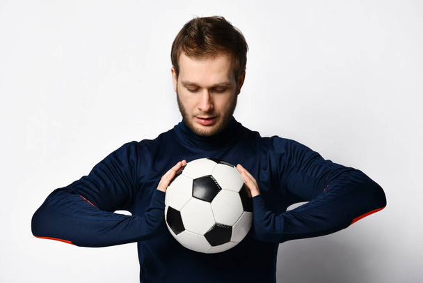 Skillful soccer player in blue tracksuit is smiling and holding a ball, posing isolated on white studio background. Close up - Фото, зображення