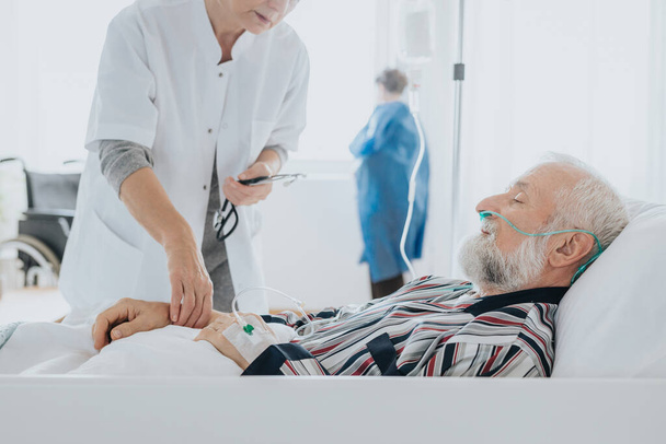 Doctor checking older dying man's pulse in the hospital - Valokuva, kuva
