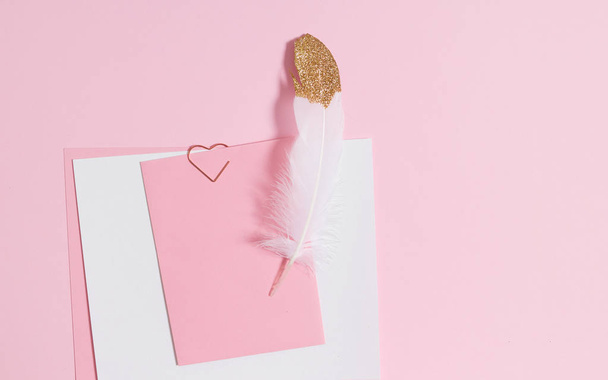 Empty template for romantic letters on a pink background. White feather with gold plating. Real photo, flat lay. Copy space for text. - Photo, Image