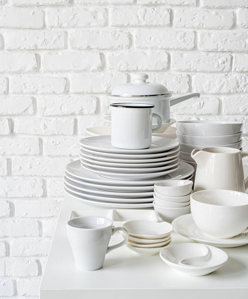 pilhas de pratos de cerâmica branca e utensílios de mesa sobre a mesa no fundo da parede de tijolo branco com espaço de cópia
 - Foto, Imagem