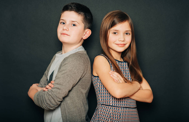 Studio portrét dvou roztomilých dětí, stojící zády k sobě, ruce zkřížené, pózující na černém pozadí - Fotografie, Obrázek