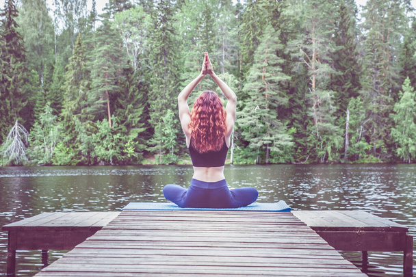 Giovane ragazza yogi praticare yoga, seduto in variazione di Gomukhasana, Mucca Viso Postura sul molo di un bellissimo lago. Concetto di vita sana ed equilibrio naturale
  - Foto, immagini