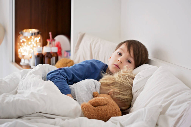 Sick children, toddler and older boy, brothers, lying in bed with a fever, resting - Foto, Bild