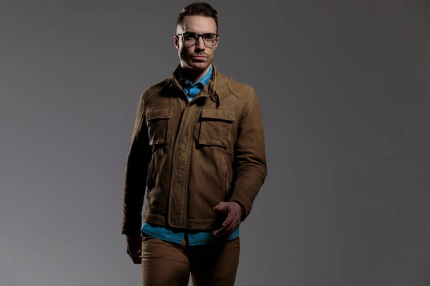 Modèle de mode déterminé portant des lunettes et une veste en cuir, marchant sur fond gris
 - Photo, image
