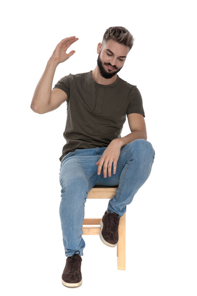 Molesto hombre casual pensar y hacer gestos mientras está sentado en una silla en fondo blanco estudio
 - Foto, Imagen