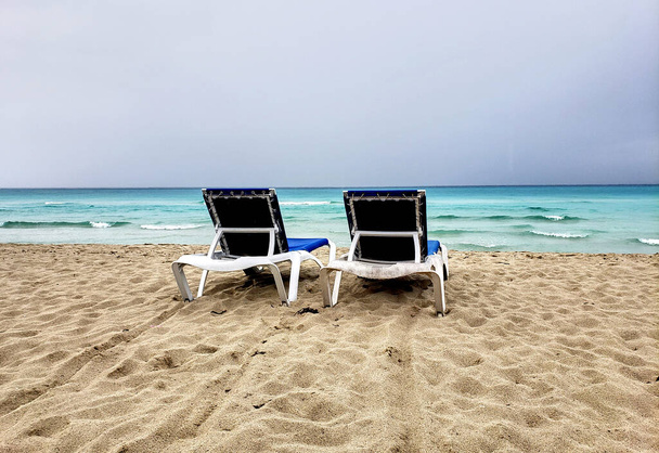 Dos tumbonas, tumbonas en una playa cubana antes de la tormenta. Clima nublado y ventoso y cielo
. - Foto, imagen