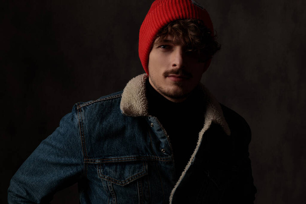 黒い背景に赤い帽子とデニムのジャケットを着たセクシーな若い男 - 写真・画像