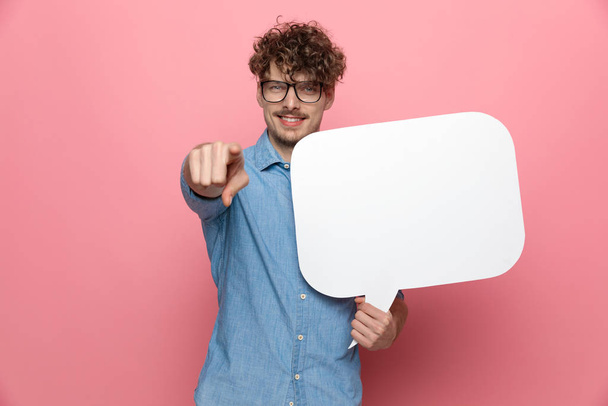 happy casual guy holding speech bubble and pointing finger, standing on pink background - Fotó, kép