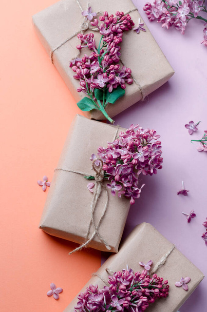 Handmade gift boxes wrapped in kraft brown paper decorated with purple lilac flowers on a pink background. Creative spring holidays background. - Foto, imagen