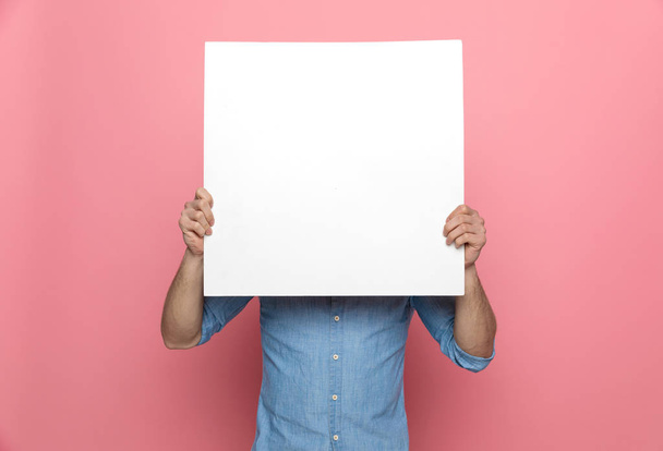 junger lässiger Kerl versteckt sich hinter leerem Brett und steht auf rosa Hintergrund - Foto, Bild